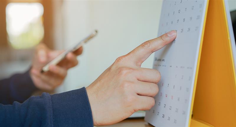 Pessoa apontando para um calendário enquanto segura um celular